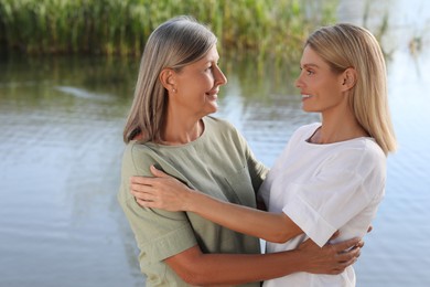 Family portrait of happy mother and daughter hugging near pond. Space for text