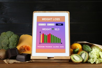 Photo of Tablet with weight loss calculator application and food products on wooden table