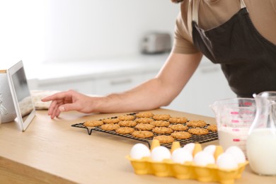 Man with freshly baked cookies watching online cooking course via tablet in kitchen, closeup