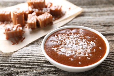 Photo of Caramel sauce with sea salt in bowl on wooden table, closeup