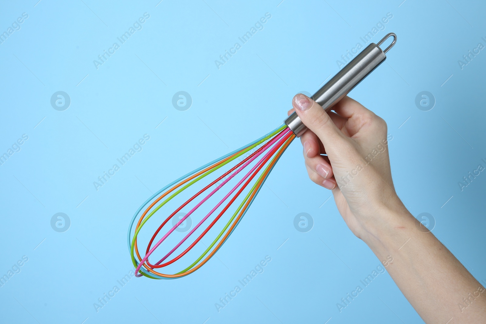 Photo of Woman holding colorful whisk on light blue background, closeup