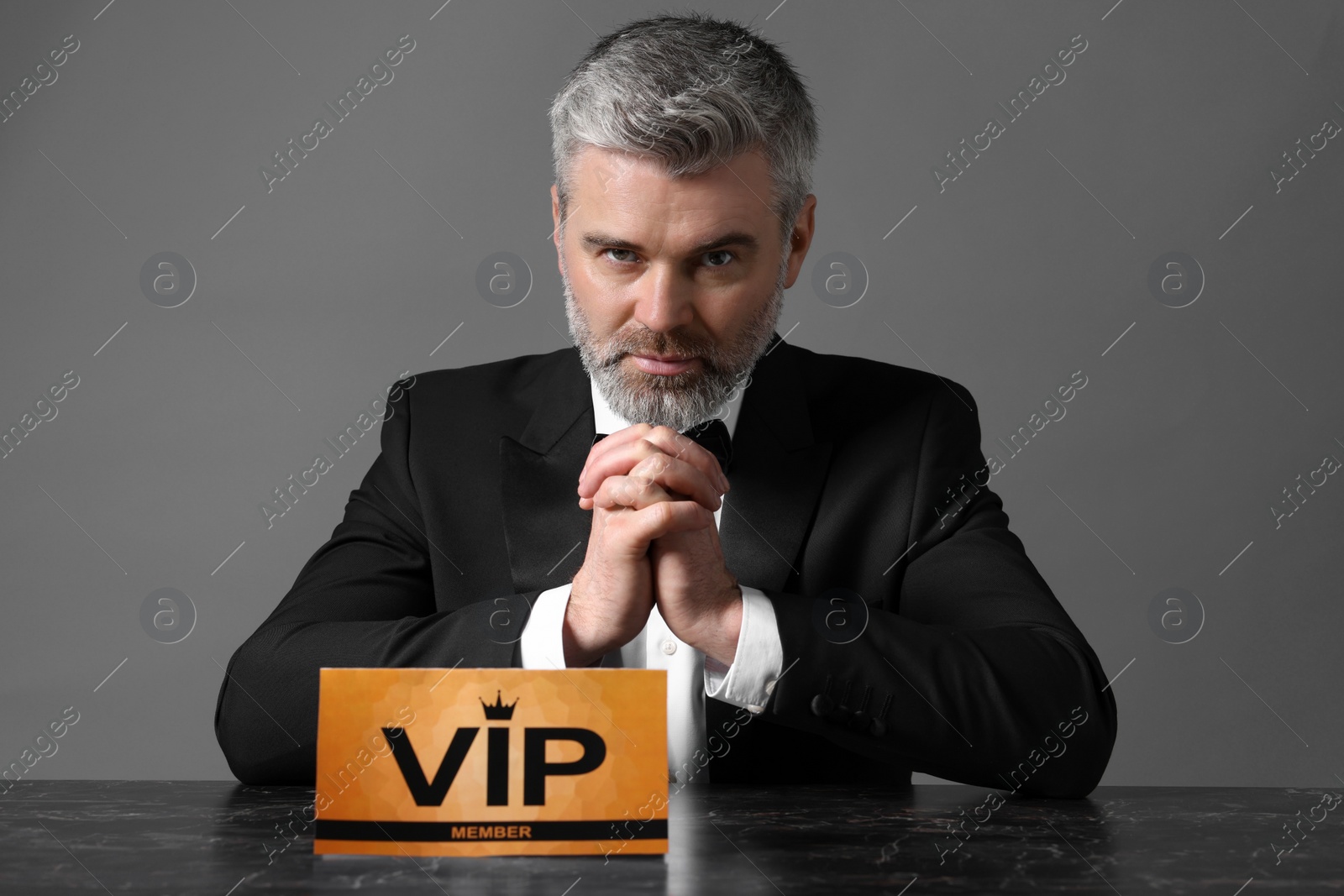 Photo of Handsome man sitting at table with VIP sign on grey background