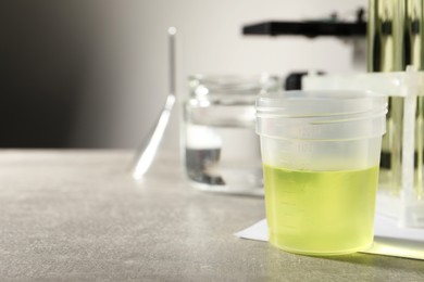 Photo of Container with urine sample for analysis and glassware on grey table, space for text