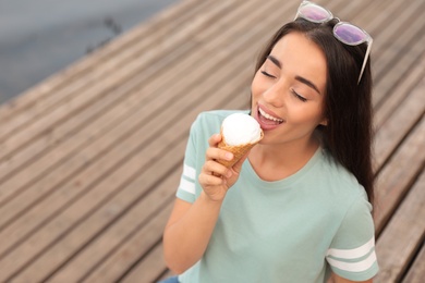 Photo of Happy young woman with delicious ice cream in waffle cone outdoors. Space for text