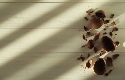 Photo of Broken and whole chocolate eggs on white wooden table, flat lay. Space for text