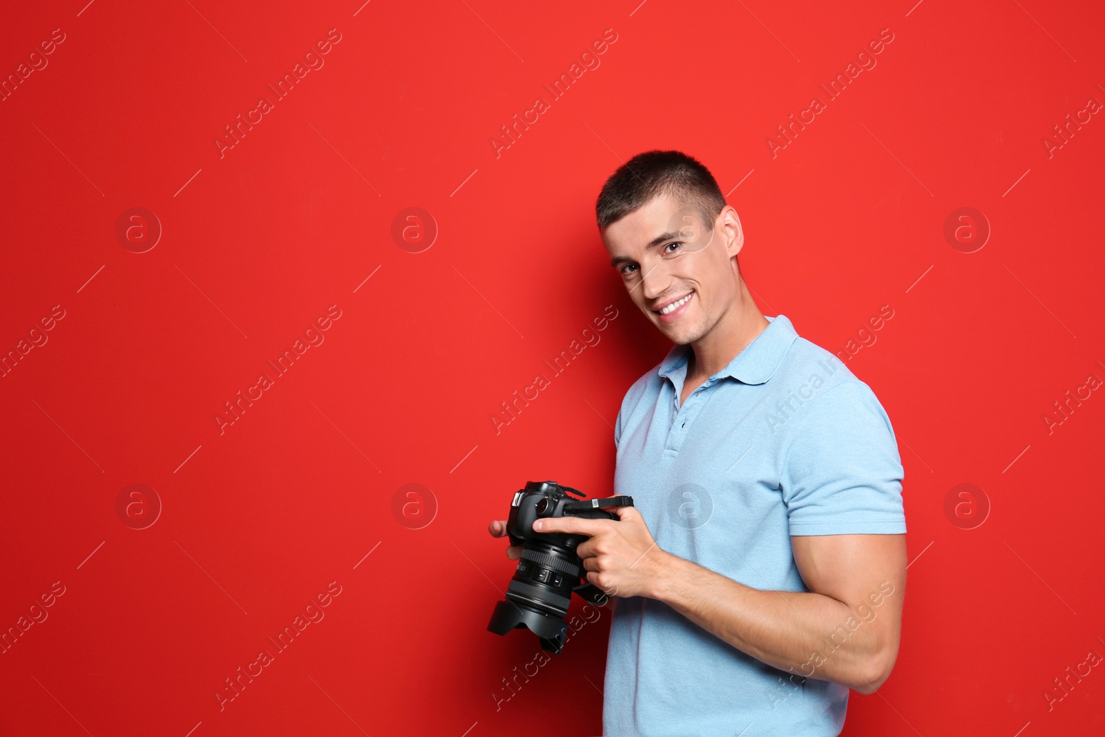 Photo of Young photographer with professional camera on red background. Space for text