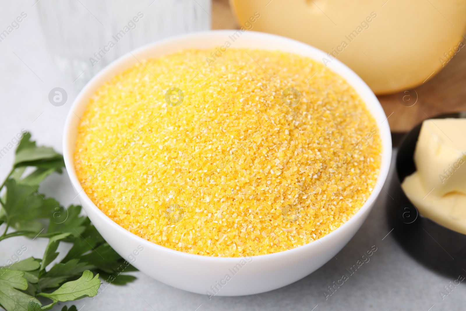 Photo of Raw cornmeal in bowl and parsley on light table, closeup