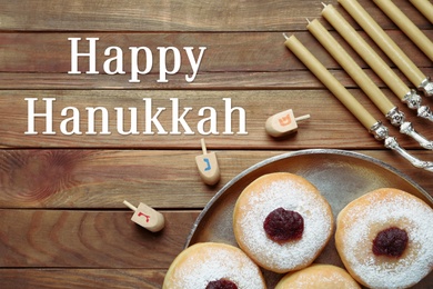 Image of Happy Hanukkah. Flat lay composition with menorah, yellow candles, dreidels and sufganiyot on wooden table