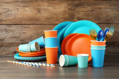 Photo of Set of bright disposable tableware on wooden table