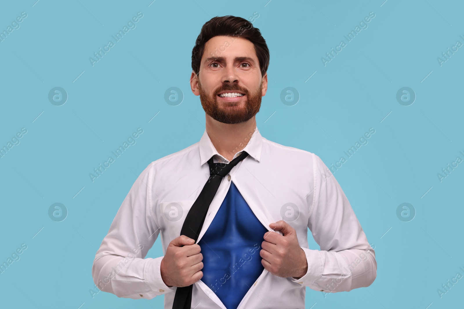 Image of Happy businessman wearing superhero costume under suit on light blue background