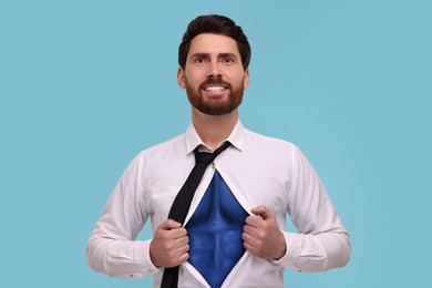 Happy businessman wearing superhero costume under suit on light blue background