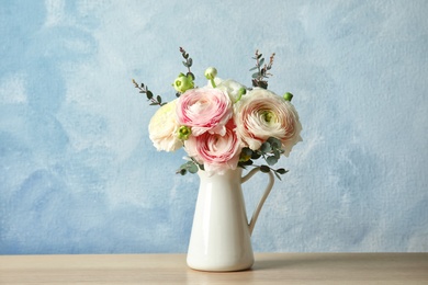 Photo of Vase with beautiful spring ranunculus flowers on table against color background