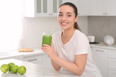 Photo of Beautiful young woman holding mason jar with delicious smoothie in kitchen