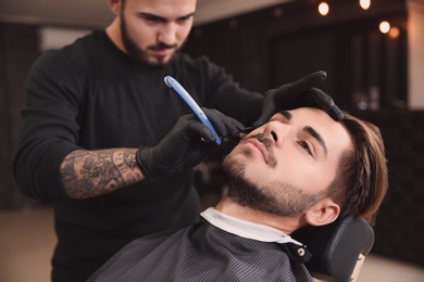 Photo of Professional hairdresser shaving client with straight razor in barbershop