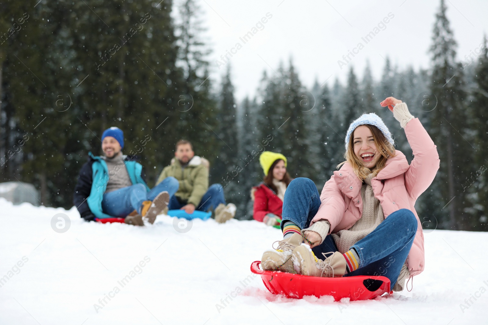 Photo of Happy friends sliding on sleds outdoors. Winter vacation