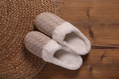 Photo of Pair of warm stylish slippers and wicker mat on wooden floor, flat lay