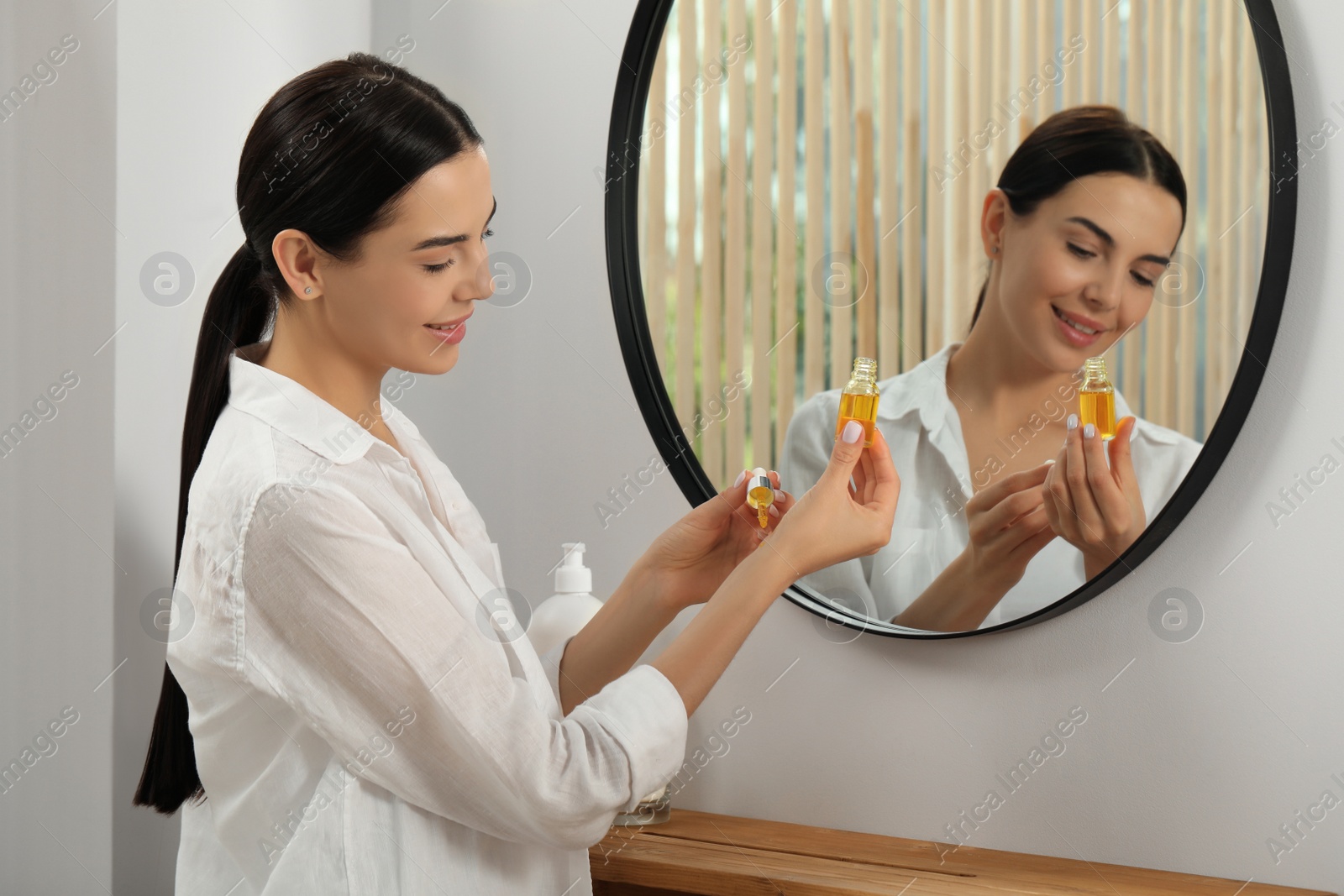 Photo of Young woman applying essential oil on wrist indoors