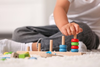 Photo of Motor skills development. Little boy playing with stacking and counting game on floor indoors, closeup