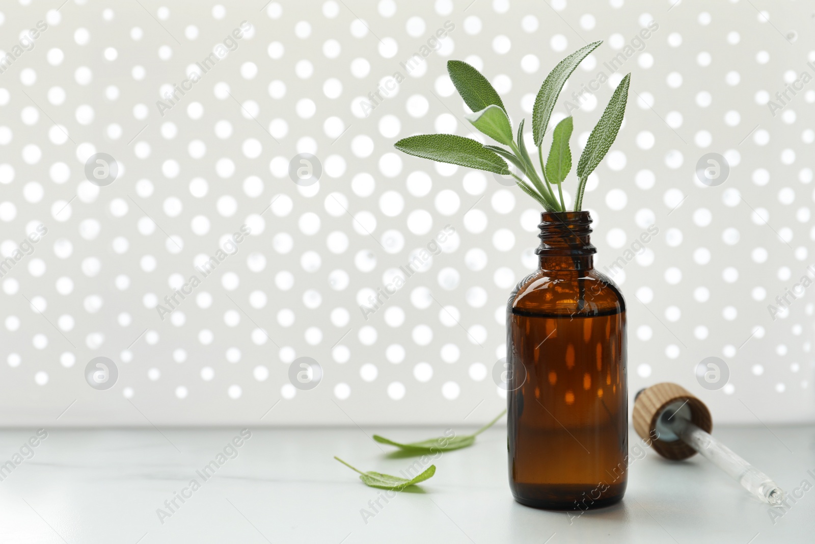 Photo of Bottle of sage essential oil and fresh herb on white table, space for text