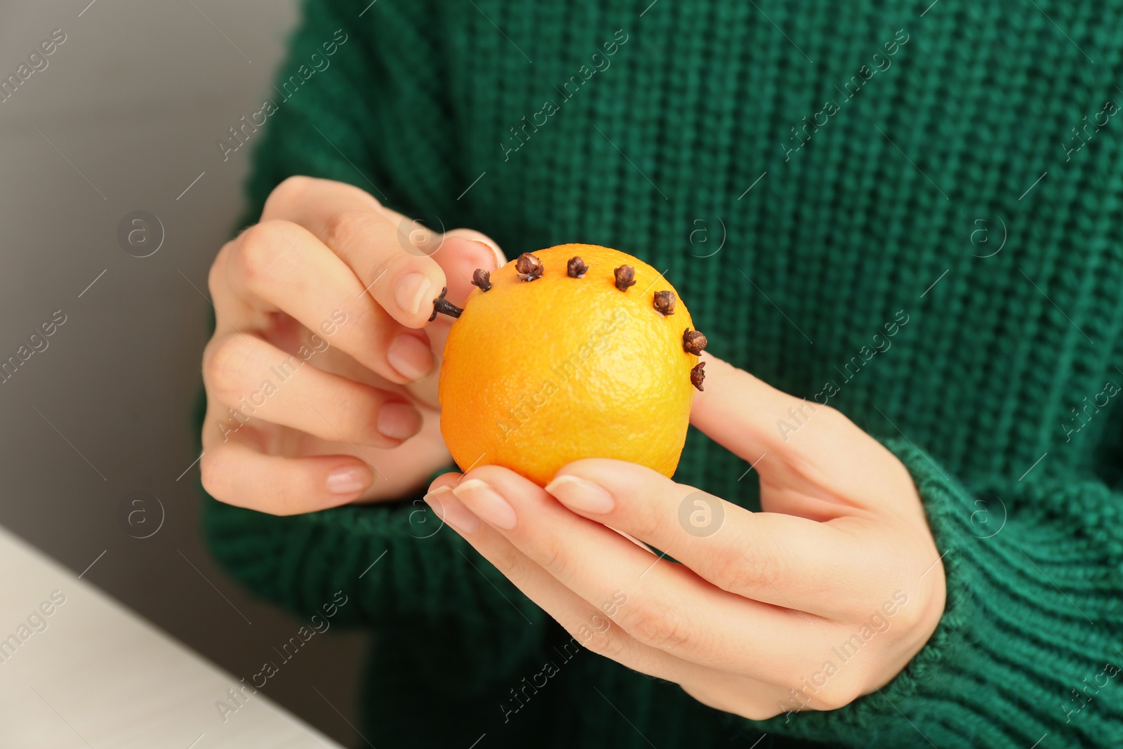 Photo of Woman decorating fresh tangerine with cloves, closeup. Making Christmas pomander ball