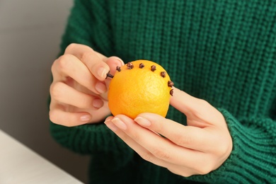 Woman decorating fresh tangerine with cloves, closeup. Making Christmas pomander ball