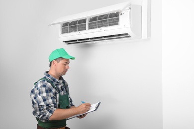 Photo of Technician with clipboard near air conditioner indoors
