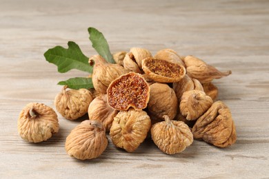 Photo of Tasty dried figs and green leaf on light wooden table