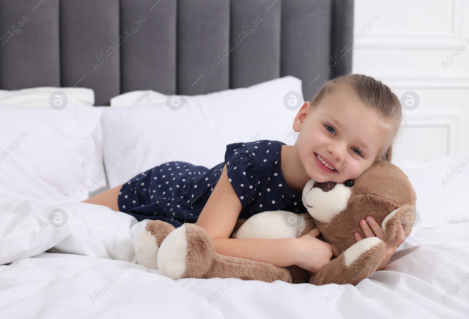 Photo of Cute little girl with teddy bear on bed