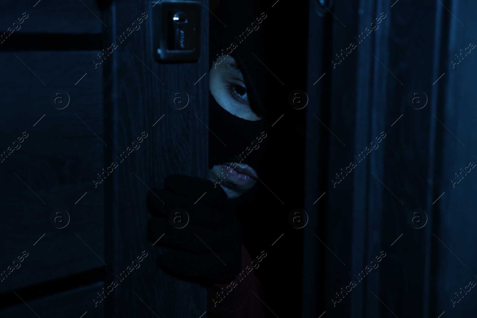 Photo of Thief in balaclava entering foreign house at night. Burglary