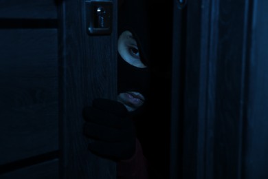 Photo of Thief in balaclava entering foreign house at night. Burglary