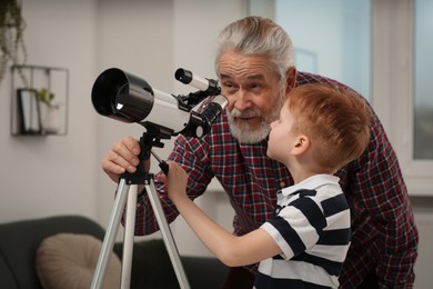 Photo of Senior man with his little grandson looking at stars through telescope in room