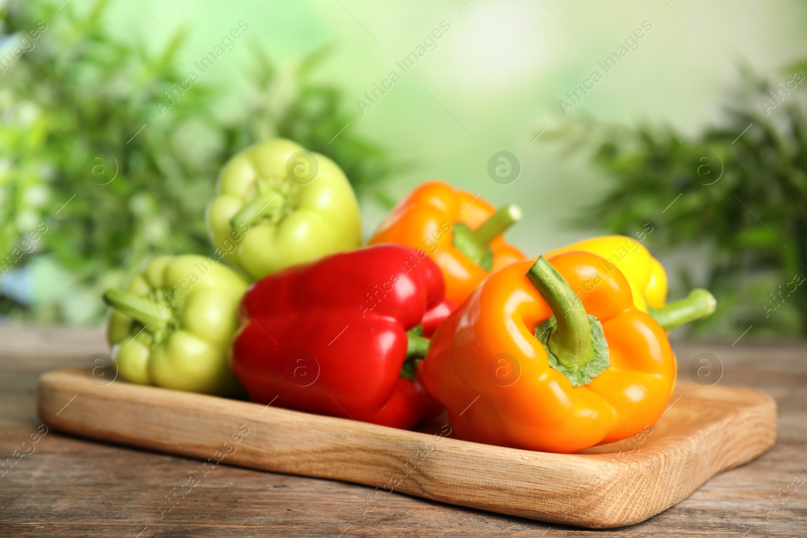 Photo of Board with ripe bell peppers on wooden table against blurred background