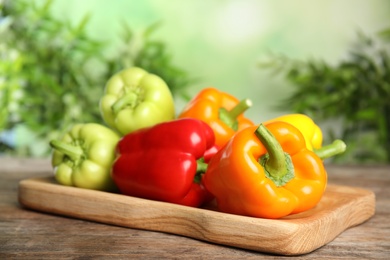 Photo of Board with ripe bell peppers on wooden table against blurred background