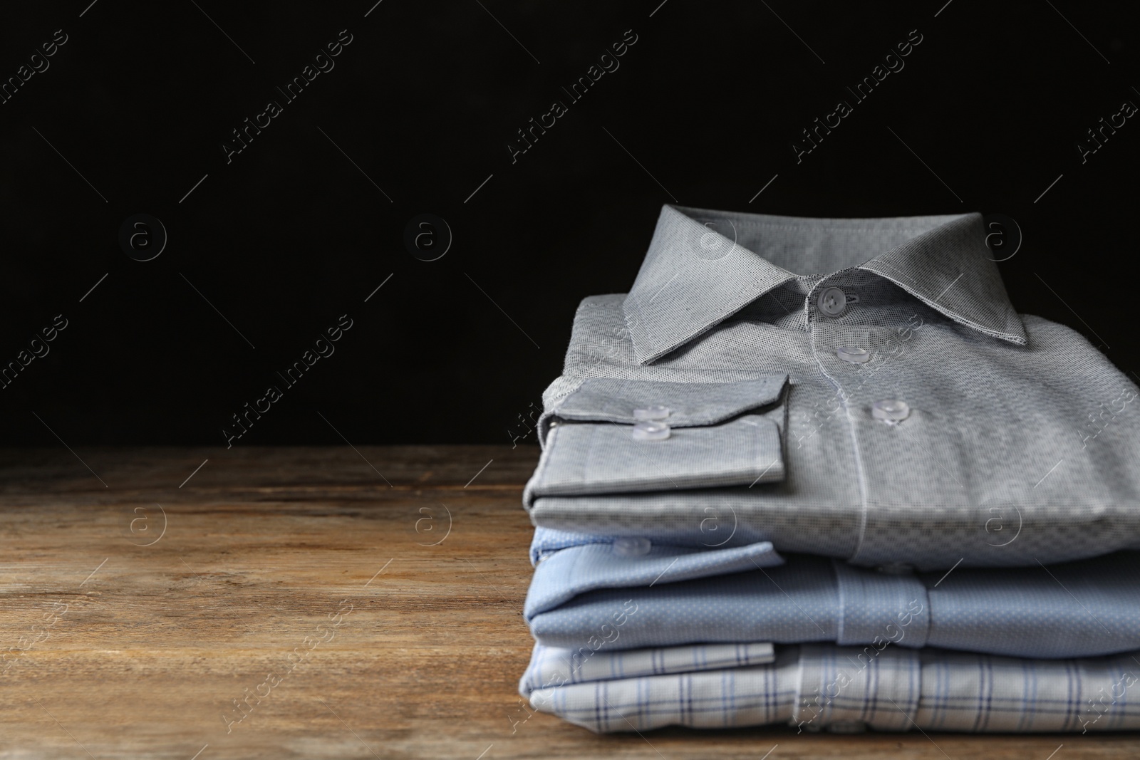 Photo of Stack of classic shirts on wooden table. Space for text