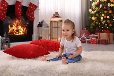 Photo of Cute little girl on floor in room decorated for Christmas