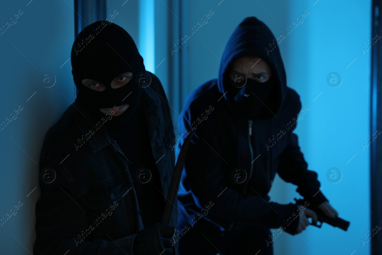 Photo of Dangerous criminals with gun and crow bar in hallway