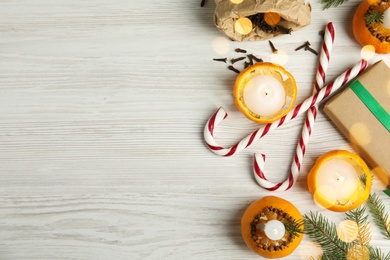 Flat lay composition with burning candles in tangerine peels as holders on white wooden table, space for text