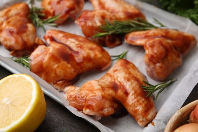 Raw marinated chicken wings, rosemary and lemon on table, closeup