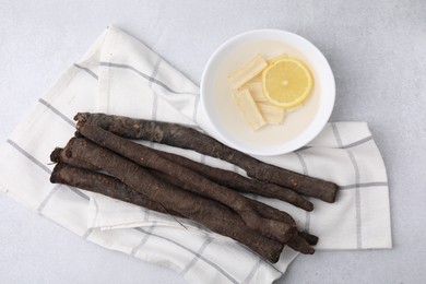 Photo of Raw salsify roots and bowl with lemon on white table, flat lay