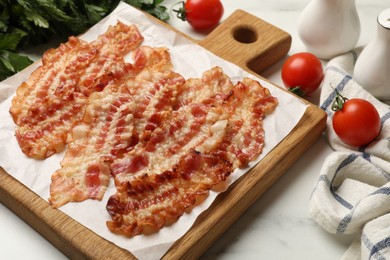 Delicious fried bacon slices and other products on white marble table, closeup