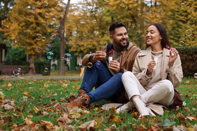 Happy young couple blowing soap bubbles in autumn park, space for text