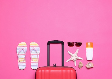 Red suitcase and beach objects on pink background, flat lay. Space for text