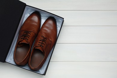 Photo of Pair of stylish leather shoes in black box on white wooden background, top view. Space for text
