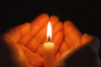 Photo of Young person holding burning candle in darkness, closeup