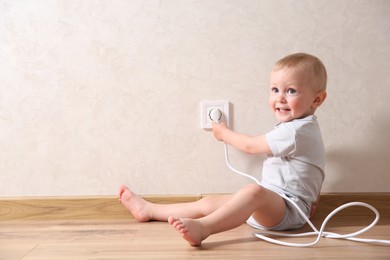 Photo of Little child playing with electrical socket and plug indoors, space for text. Dangerous situation