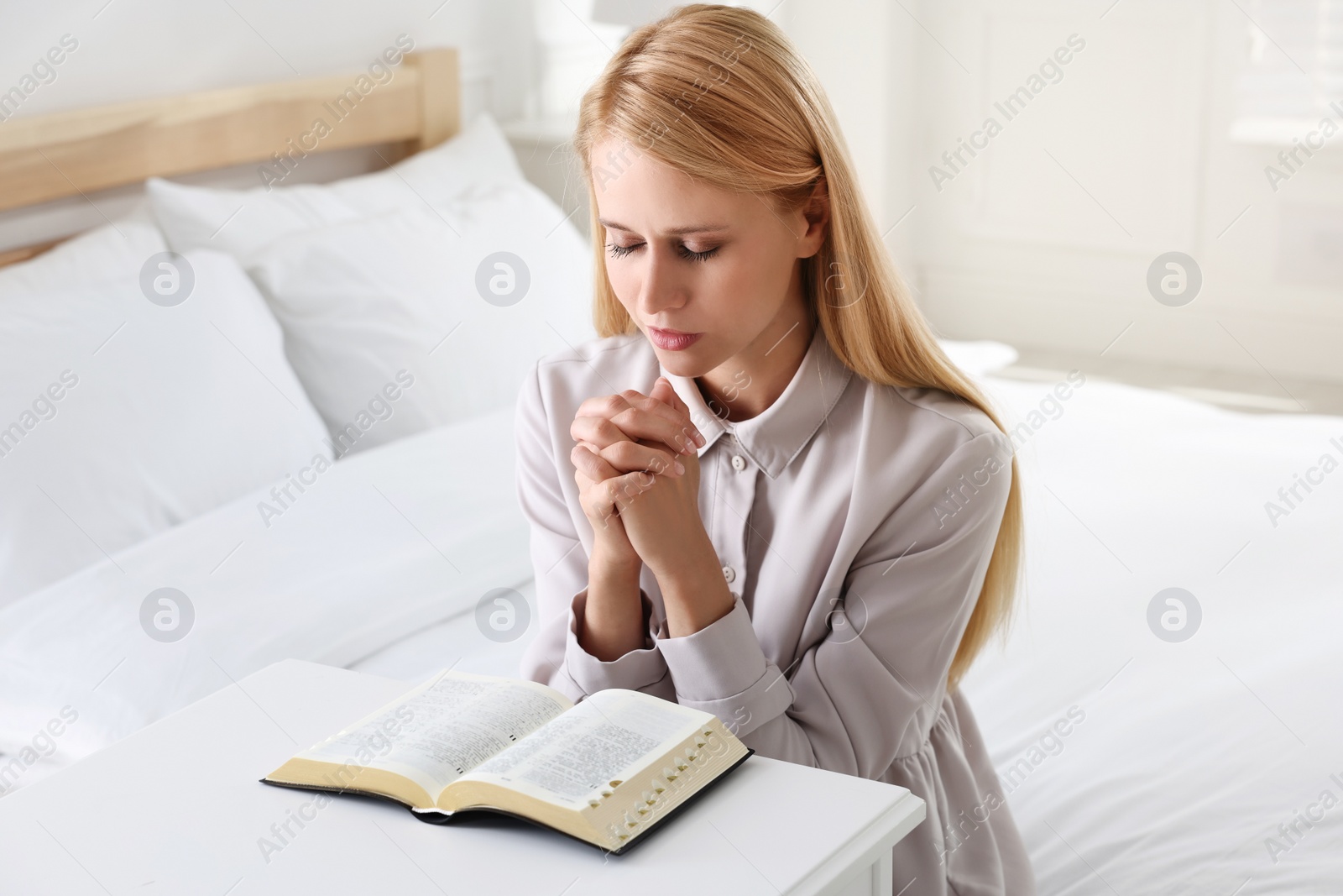 Photo of Religious young woman with Bible praying in bedroom