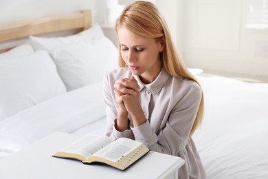 Photo of Religious young woman with Bible praying in bedroom