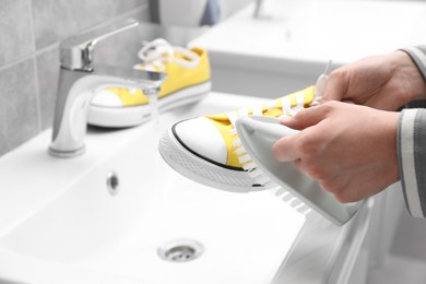 Photo of Woman washing stylish sneakers with brush in sink, closeup