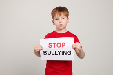 Boy holding sign with phrase Stop Bullying on light grey background