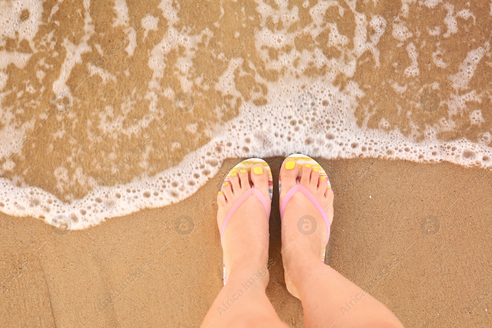 Photo of Top view of woman with stylish flip flops on sand near sea, space for text. Beach accessories